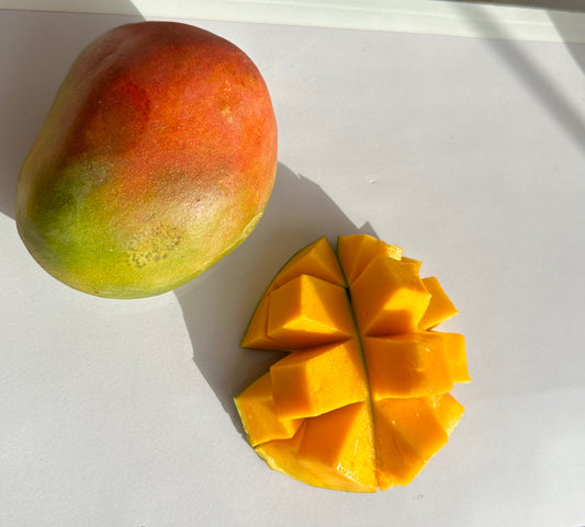 Yvaya farm - two ripe mangoes, with one half cut and fanned out into a hedgehog style on a bright, sunlit surface.